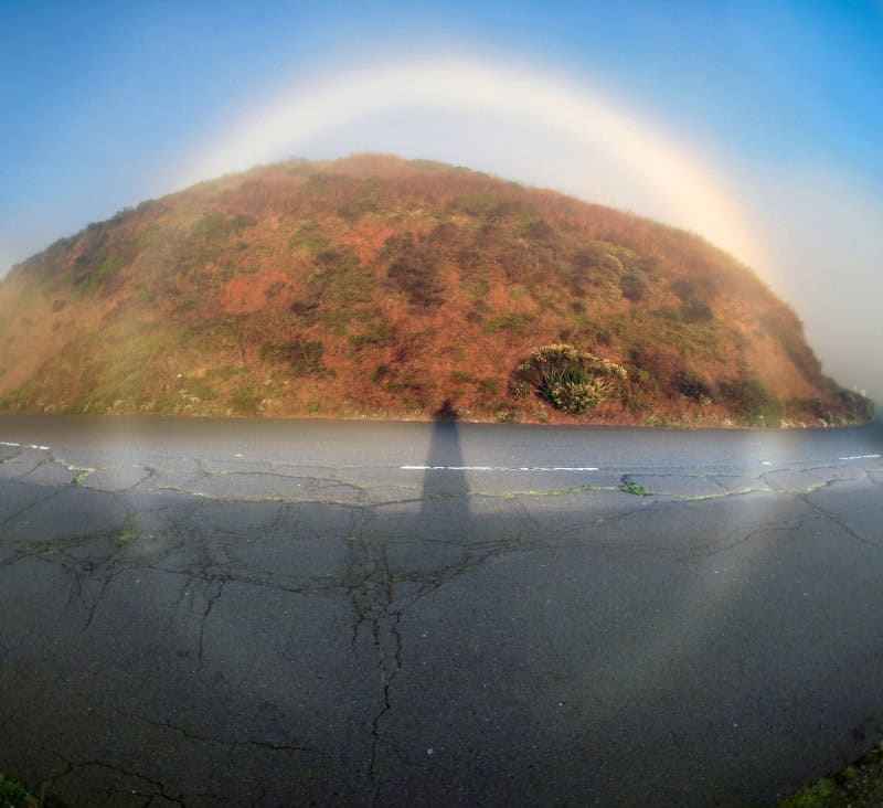 White fog bow arching over a misty landscape, a rainbow without colour