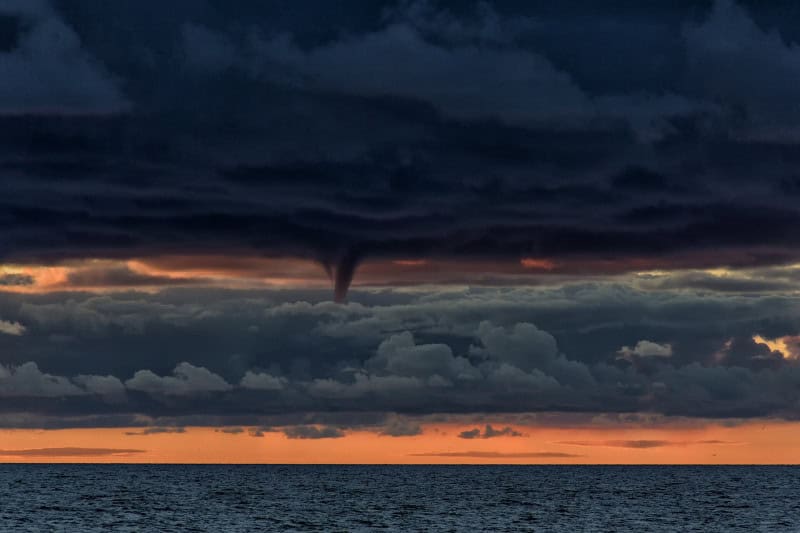 Rotating cone-shaped funnel cloud descending from a storm base without reaching the ground