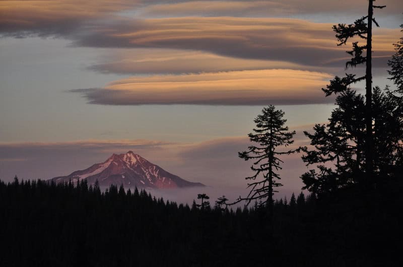 Smooth lens-shaped lenticular cloud stacked over a mountain peak, resembling a flying saucer