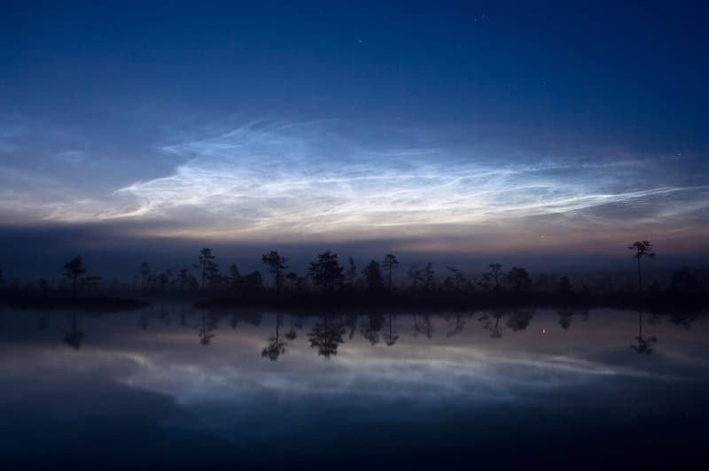 Electric blue noctilucent clouds glowing in a deep twilight sky after sunset