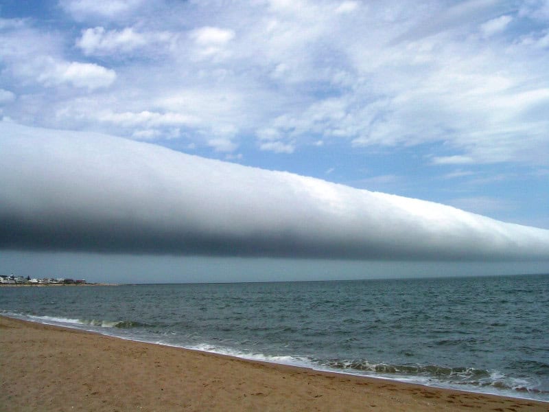 Detached horizontal tube-shaped roll cloud stretching across the horizon above open water