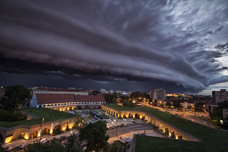 Low wedge-shaped shelf cloud advancing across a city skyline ahead of a thunderstorm