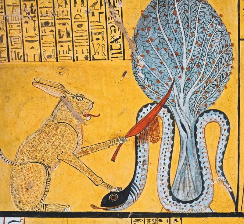 Egyptian tomb painting on a yellow ground of a spotted cat cutting into a large coiled serpent beneath a tree