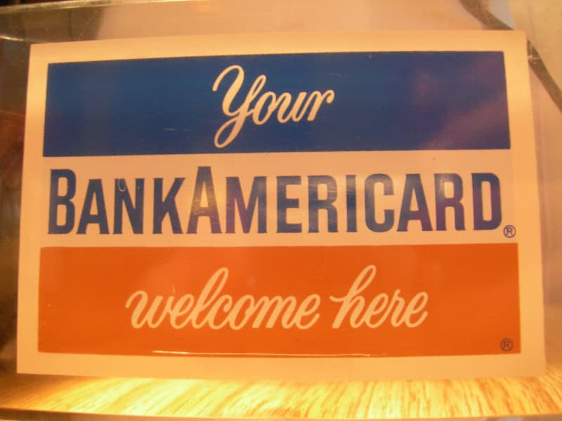 A blue, white and orange merchant sign reading "Your BankAmericard welcome here"