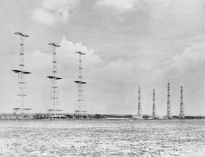 A Chain Home radar station in an open field: three tall steel lattice transmitter towers with cross-arm aerials on the left and four shorter receiver towers on the right
