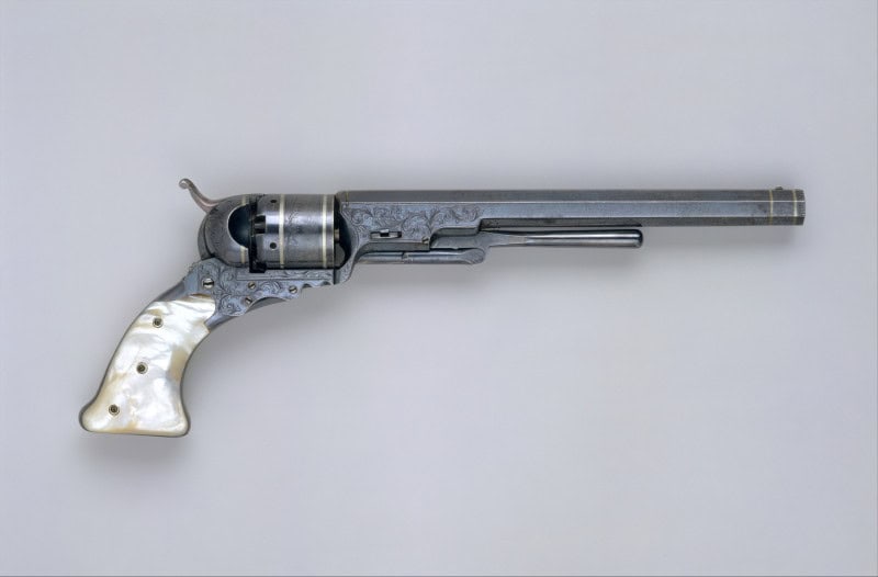 A Colt Paterson percussion revolver side-on, with a long octagonal barrel, fluted cylinder, folding trigger and iridescent pearl grip