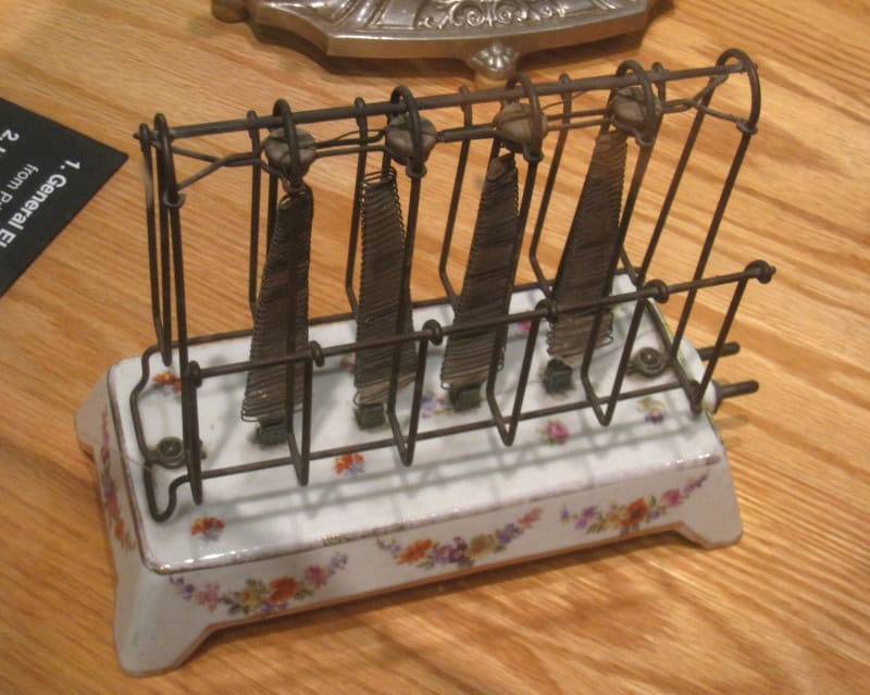 A General Electric D-12 toaster: a floral-painted white porcelain base supporting an open bent-wire cage with four flat coiled heating elements fully exposed