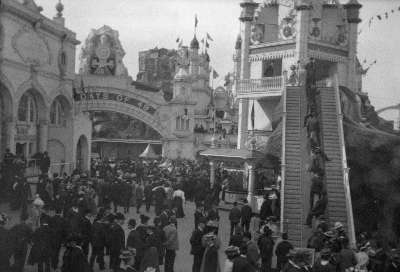 A dense straw-hatted crowd at Luna Park, Coney Island, with a steep wooden inclined moving stairway carrying seated riders at the right of the frame