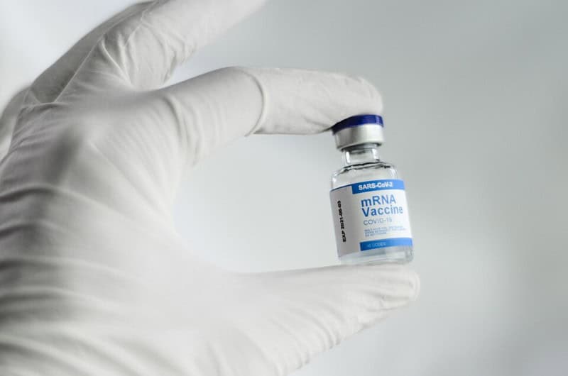 A gloved hand holding a small vial of mRNA COVID-19 vaccine