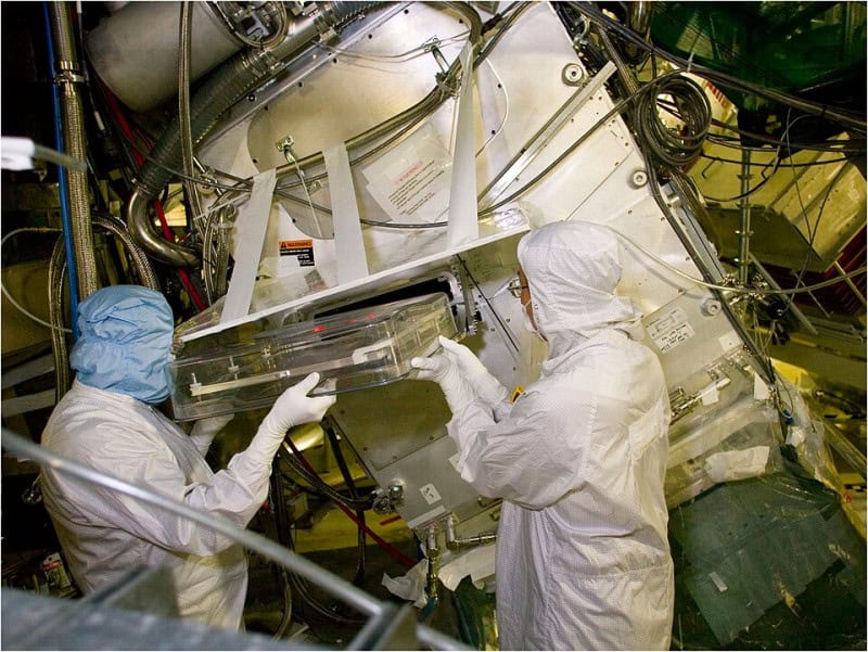 Technicians in white cleanroom suits working on equipment at the National Ignition Facility target chamber