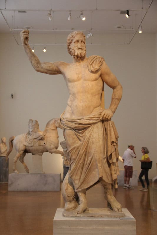 Marble Poseidon striding forward with his right arm raised to hold a missing trident, a dolphin at his feet
