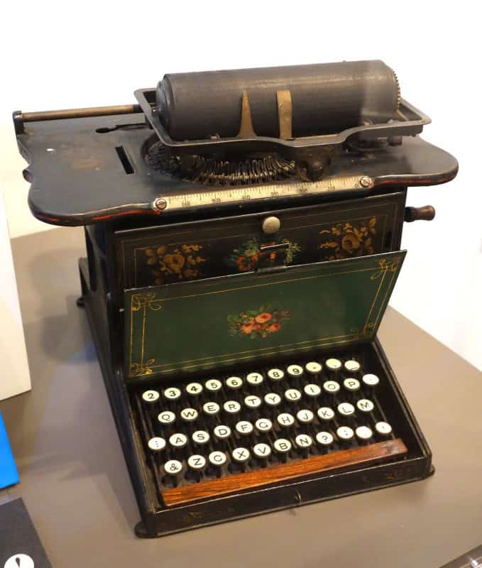 A Remington No. 1 typewriter: a black cast-iron body hand-painted with gold scrollwork and floral bouquets, four rows of round white keys, a wooden space bar and a cylindrical platen