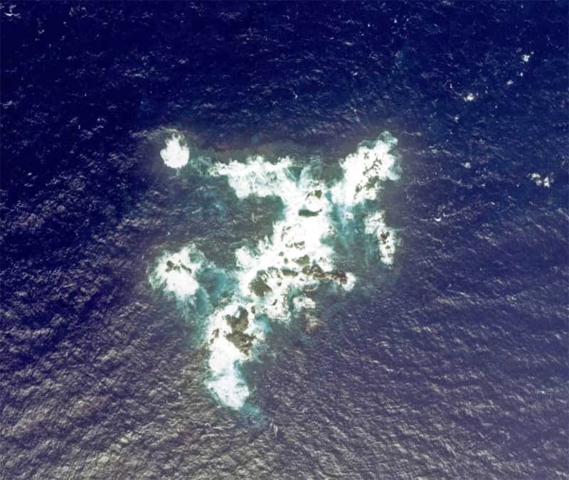 Close aerial view of the Bayonnaise Rocks with surf breaking white over black rock in a dark blue sea