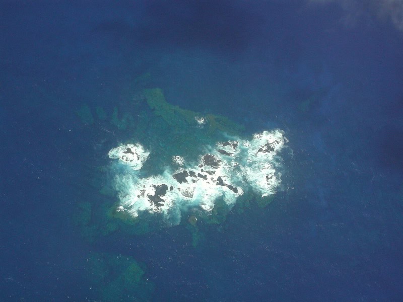 Aerial photograph from 2002 of the Bayonnaise Rocks showing pale shallow water and surf around the rocks and darker deep water beyond