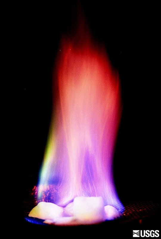 A lump of white methane hydrate ice burning with an orange and violet flame against a black background