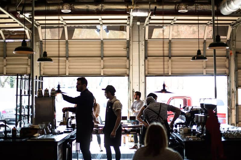 Cafe staff in aprons working behind a counter beside open garage-style doors