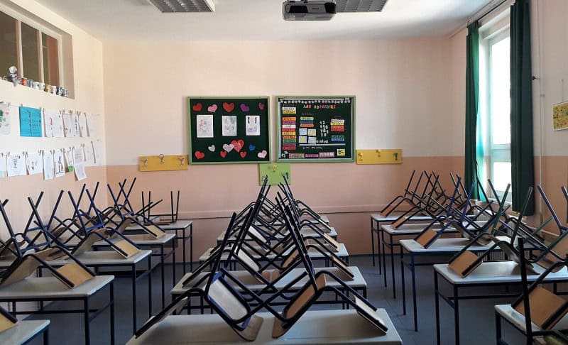 An empty classroom with chairs stacked upside down on the desks and a noticeboard at the front