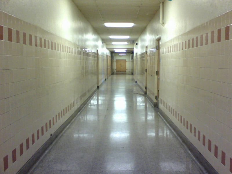 An empty high school corridor lined with lockers under overhead strip lights