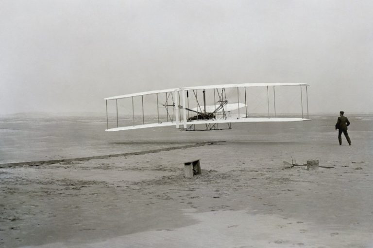 The Wright Flyer taking off at Kill Devil Hills on 17 December 1903, with Wilbur Wright running alongside