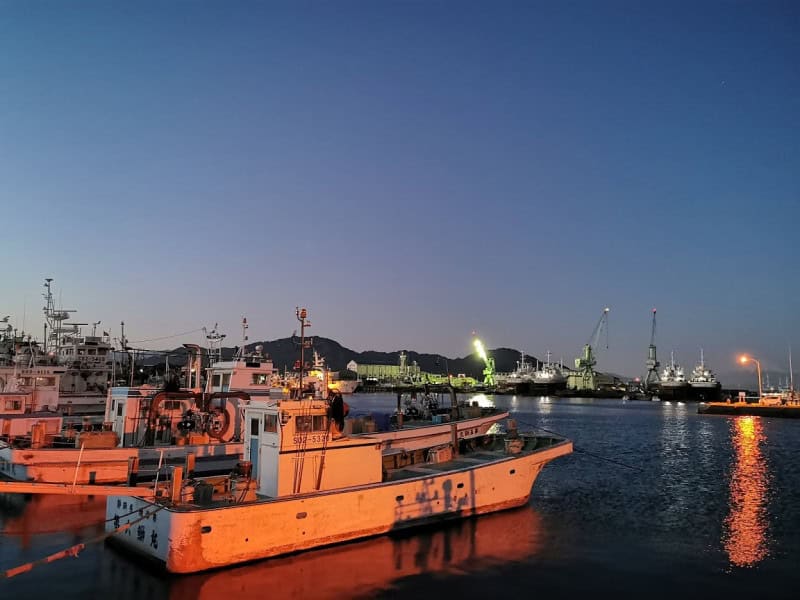 Orange-hulled fishing boats moored at Yaizu fishing port at dusk, with harbour lights and cranes in the background
