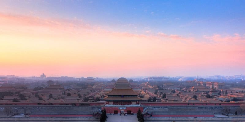 The Forbidden City in Beijing seen from Coal Hill, its rows of roofs hazy in the shade under a sunset sky