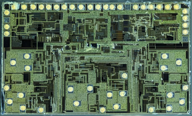 A magnified photograph of an integrated circuit die showing its green and gold circuit layers