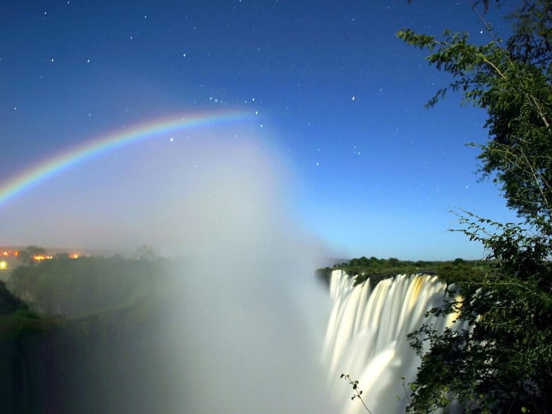 A pale moonbow arcing through the spray of Victoria Falls at night, lit by moonlight on a long exposure