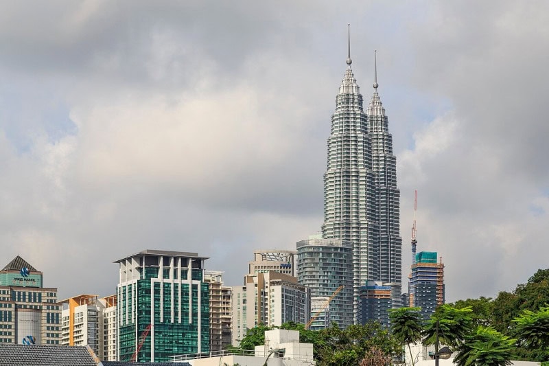 The Petronas Twin Towers in Kuala Lumpur seen at a distance above rooftops and palm trees