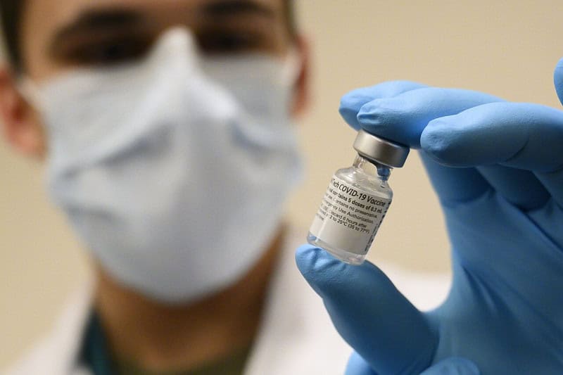 A gloved healthcare worker holding up a vial of the Pfizer-BioNTech COVID-19 mRNA vaccine