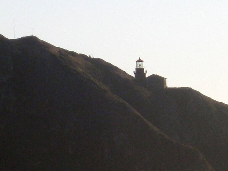 Point Sur lighthouse silhouetted on its rocky headland against a pale evening sky on the California coast