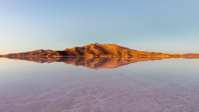 A shallow film of water on the Salar de Uyuni salt flat mirroring a low ridge and the sky above it
