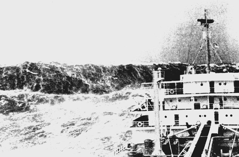 Black and white photograph from a ship in heavy seas, with a huge wave towering beside the superstructure