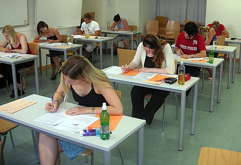 Students sitting at spaced desks writing a paper exam in a classroom