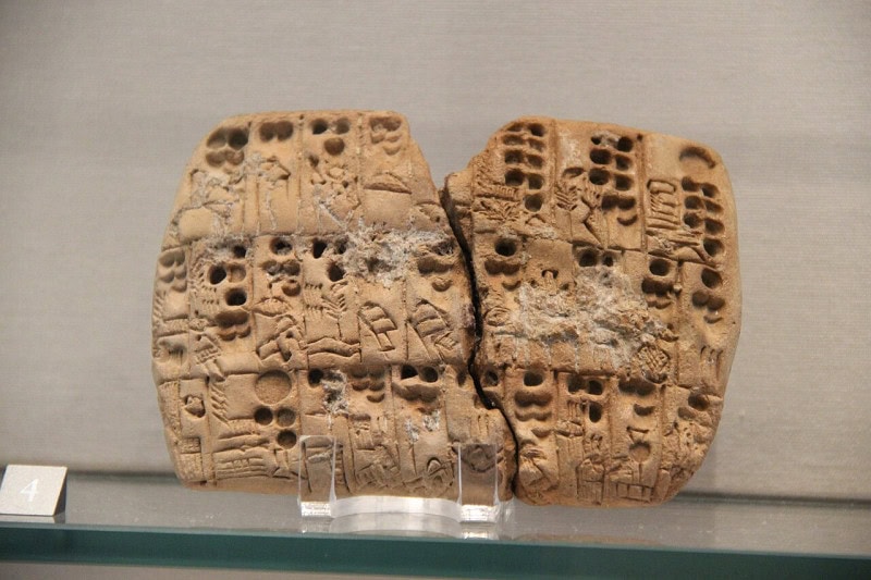 A Sumerian clay tablet covered in cuneiform writing, displayed in a museum