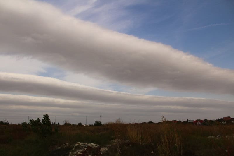Long parallel tubes of volutus cloud lying across the sky above a village and open fields