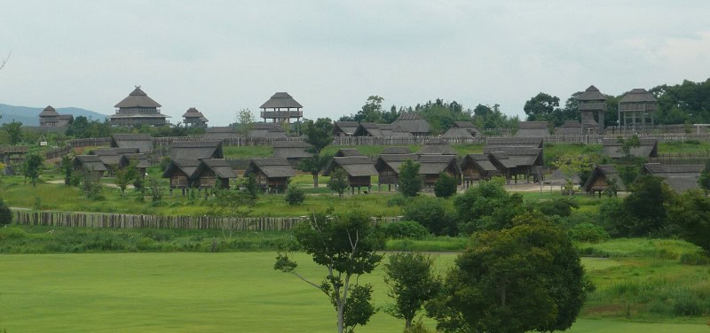 Reconstructed thatched buildings and watchtowers of the Yoshinogari Yayoi-period site on Kyushu under an overcast sky