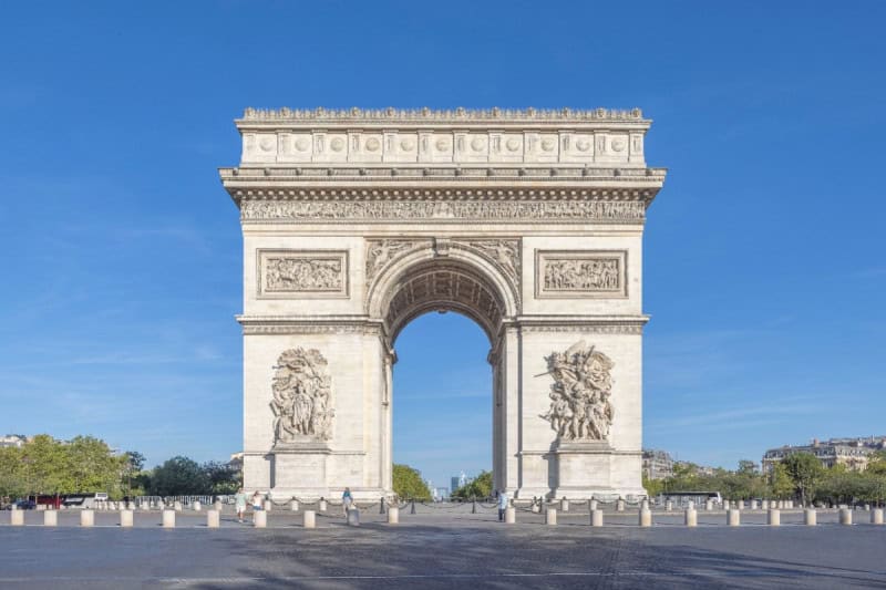 The Arc de Triomphe in Paris seen head-on across the Place Charles de Gaulle under a blue sky