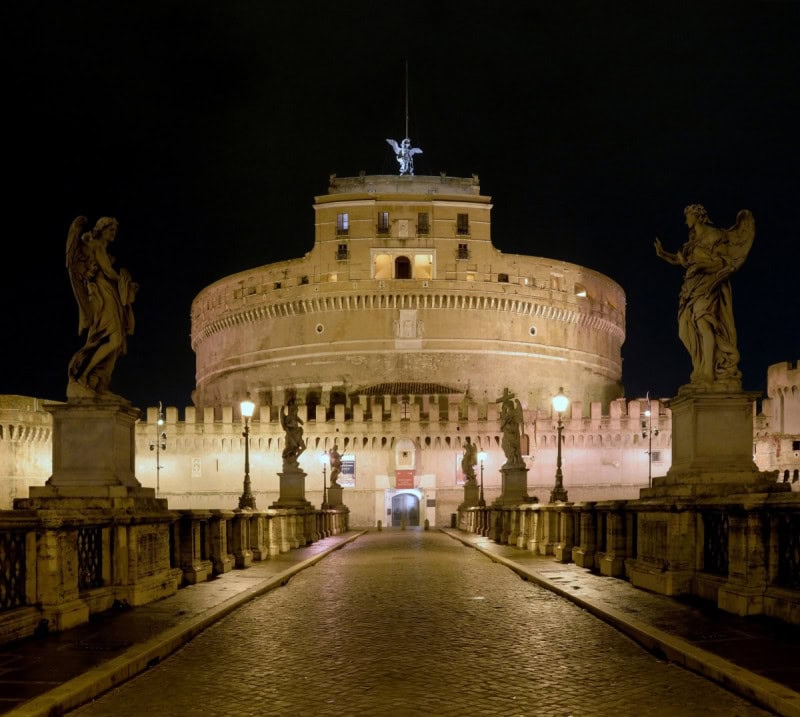 Castel Sant’Angelo in Rome lit at night, with the angel statues of the bridge in front