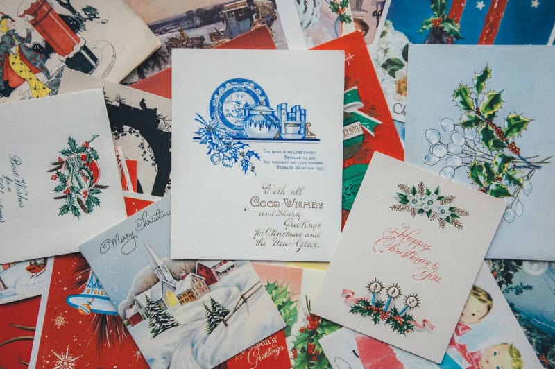 A scattered pile of vintage Christmas and holiday cards with holly and wreath illustrations