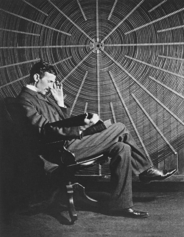 Nikola Tesla seated reading in front of the large flat spiral coil of his Tesla coil transformer in his New York laboratory, 1896
