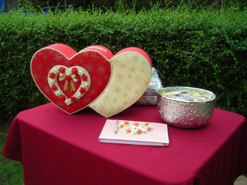 A wedding reception table with a red cloth, a heart-shaped box for guests' gift envelopes and a guest book